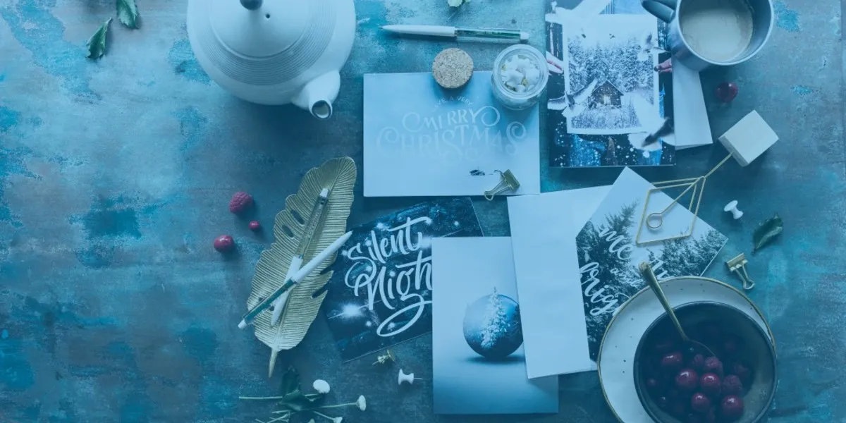 Christmas cards with messages, along with a pen, a decorative feather, a bowl of cherries, and a cup of coffee.