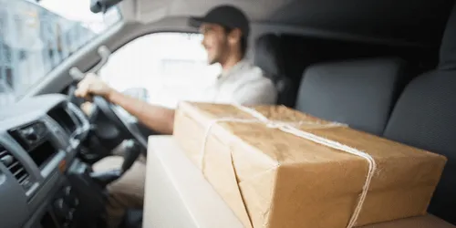 A person driving a vehicle, with a box sitting on the passenger seat