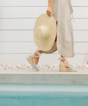 Woman holding sunhat wearing a dress walking alongside a pool