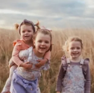 Three children standing in field, one climbing on the others back