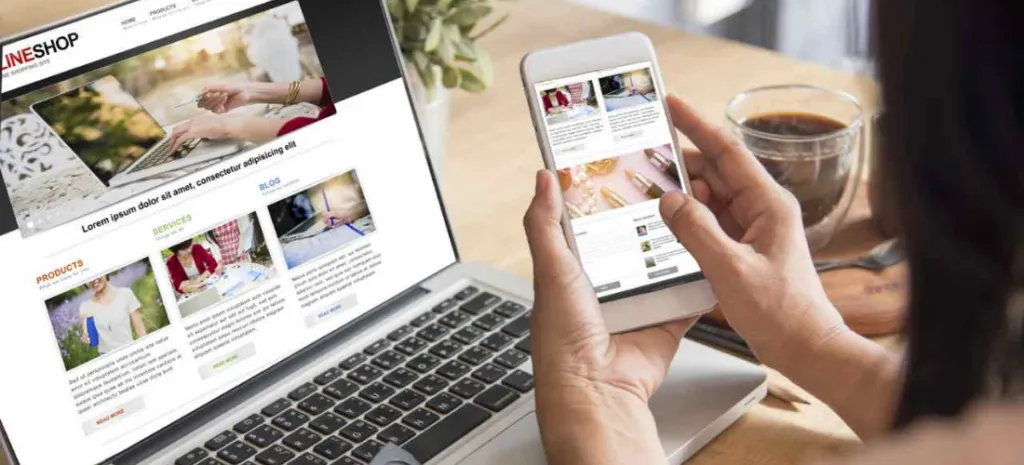 A person is using a smartphone and a laptop simultaneously to browse an online platform, with a cup of coffee nearby. Both devices display similar web content, suggesting a focus on digital or e-commerce activities.