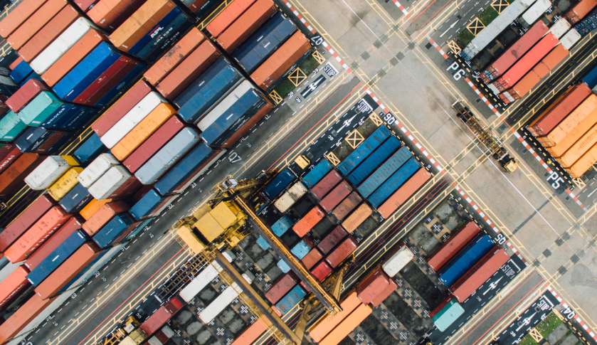 An aerial view of a shipping yard with stacked cargo containers organised in rows, showcasing various colours and sizes.