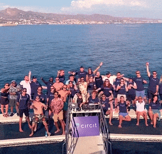 Eine Gruppe von Menschen, die auf ruhigem Wasser vor dem Hintergrund von Bergen eine Bootsparty genießen, tanzen und mit den Händen winken.