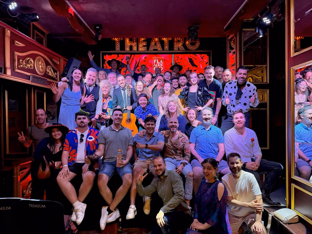 Eine große Gruppe von Menschen posiert auf der Bühne vor einem beleuchteten „THEATRO“-Schild im Teatro Flamenco.