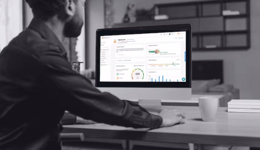 Man sitting at a table working on a desktop computer displaying business analytics dashboard with charts and metrics.