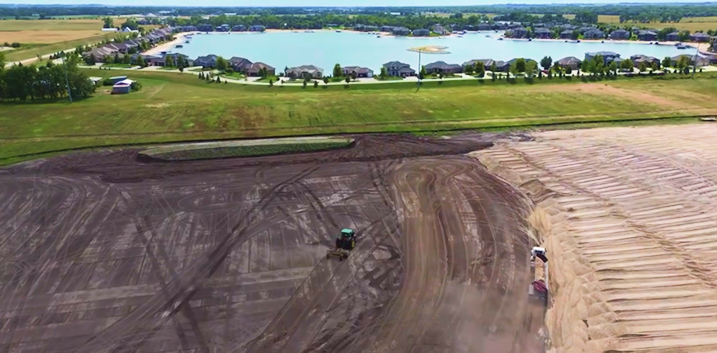 Valley, Nebraska aerial view of a large construction site with earthmoving equipment near a lake surrounded by residential houses.