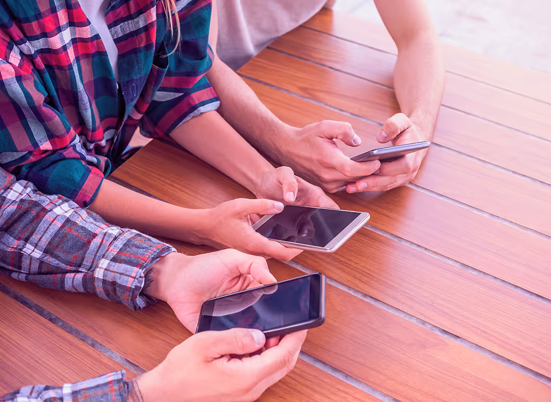A group of people sitting at a table holding smartphones, each focused on their own screen.