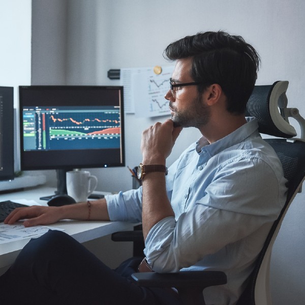 A person wearing glasses looks intently at a large screen displaying colorful data charts and graphs.