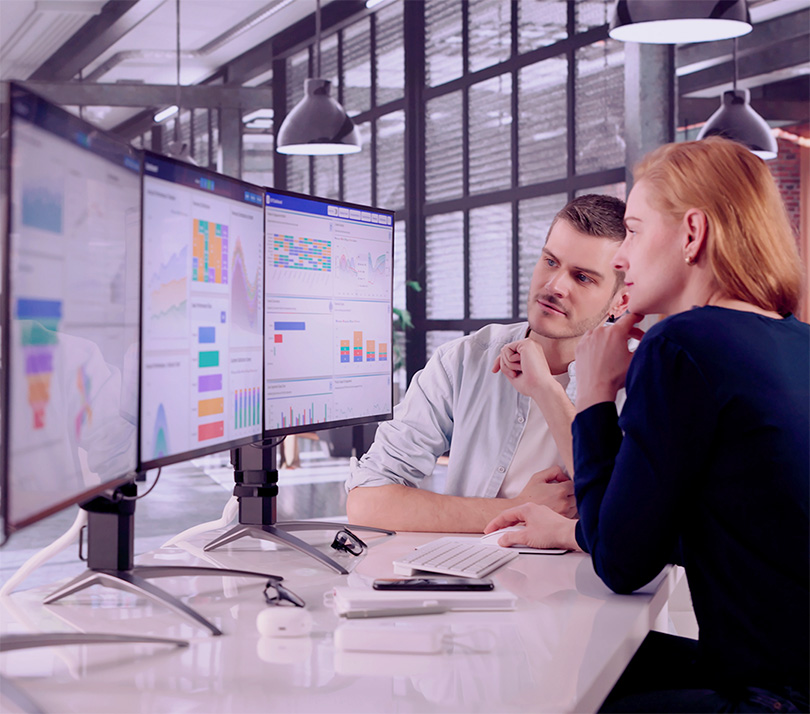 Two data analysts study a series of charts on a screen