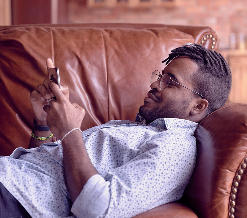 A man is looking at his smartphone while relaxing on a leather sofa at home.