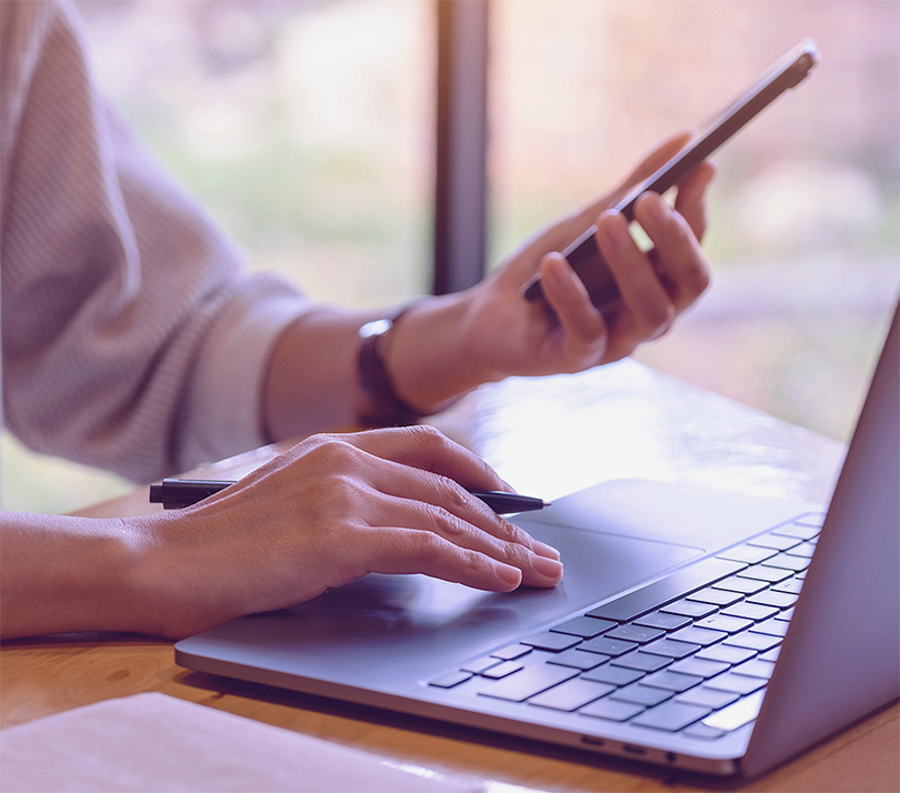 Person using a smartphone alongside a laptop