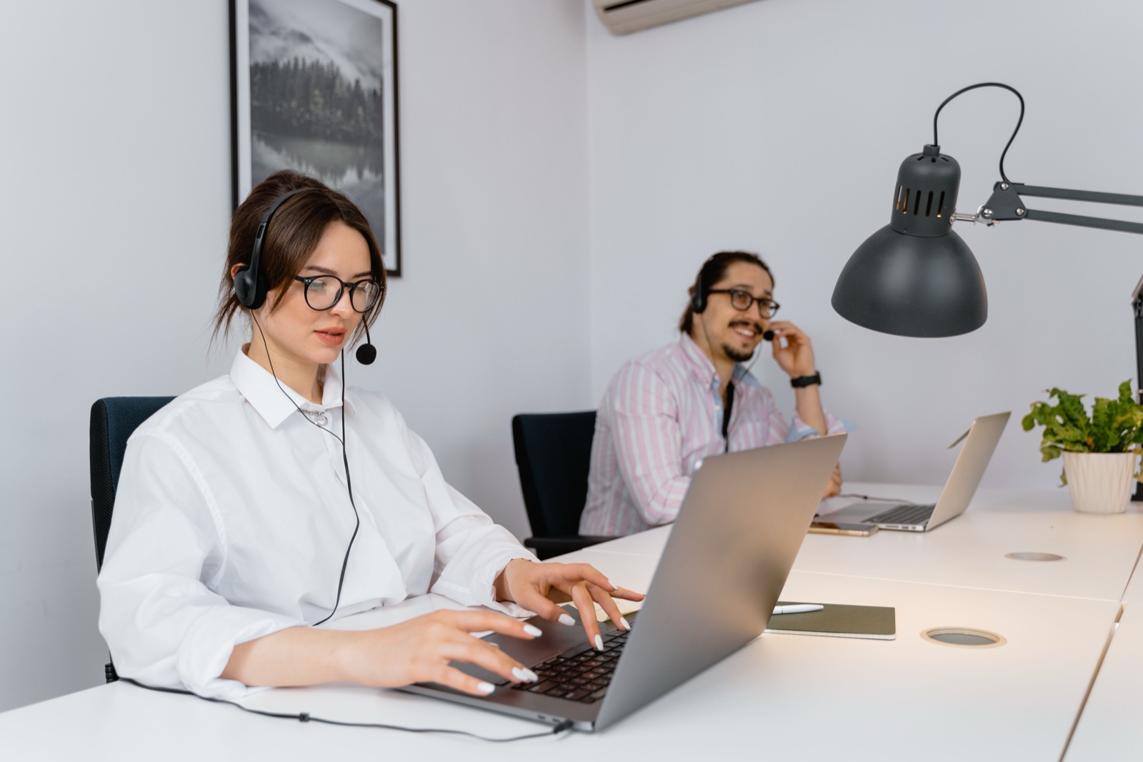 Zwei Personen mit Headset am Schreibtisch, eine telefoniert und lacht