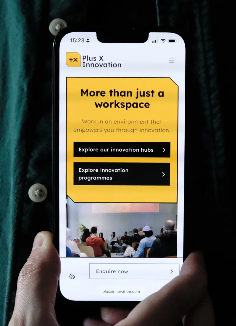 Smartphone screen showing Plus X Innovation website with a yellow banner stating 'More than just a workspace' and buttons to explore innovation hubs and programmes.
