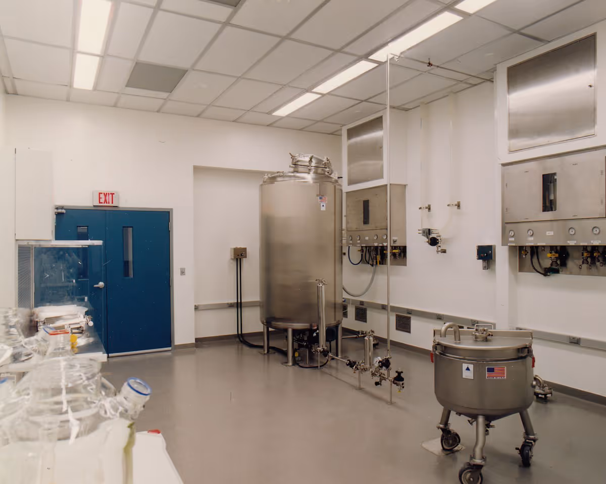 Clean industrial lab with stainless steel tanks, blue exit doors, and white walls and ceiling panels.