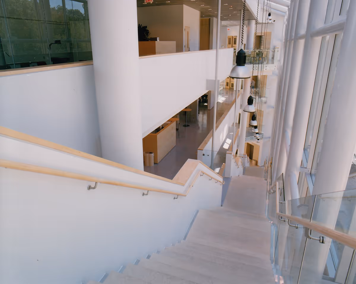 Modern interior stairway with wooden handrails, large windows, and hanging pendant lights.