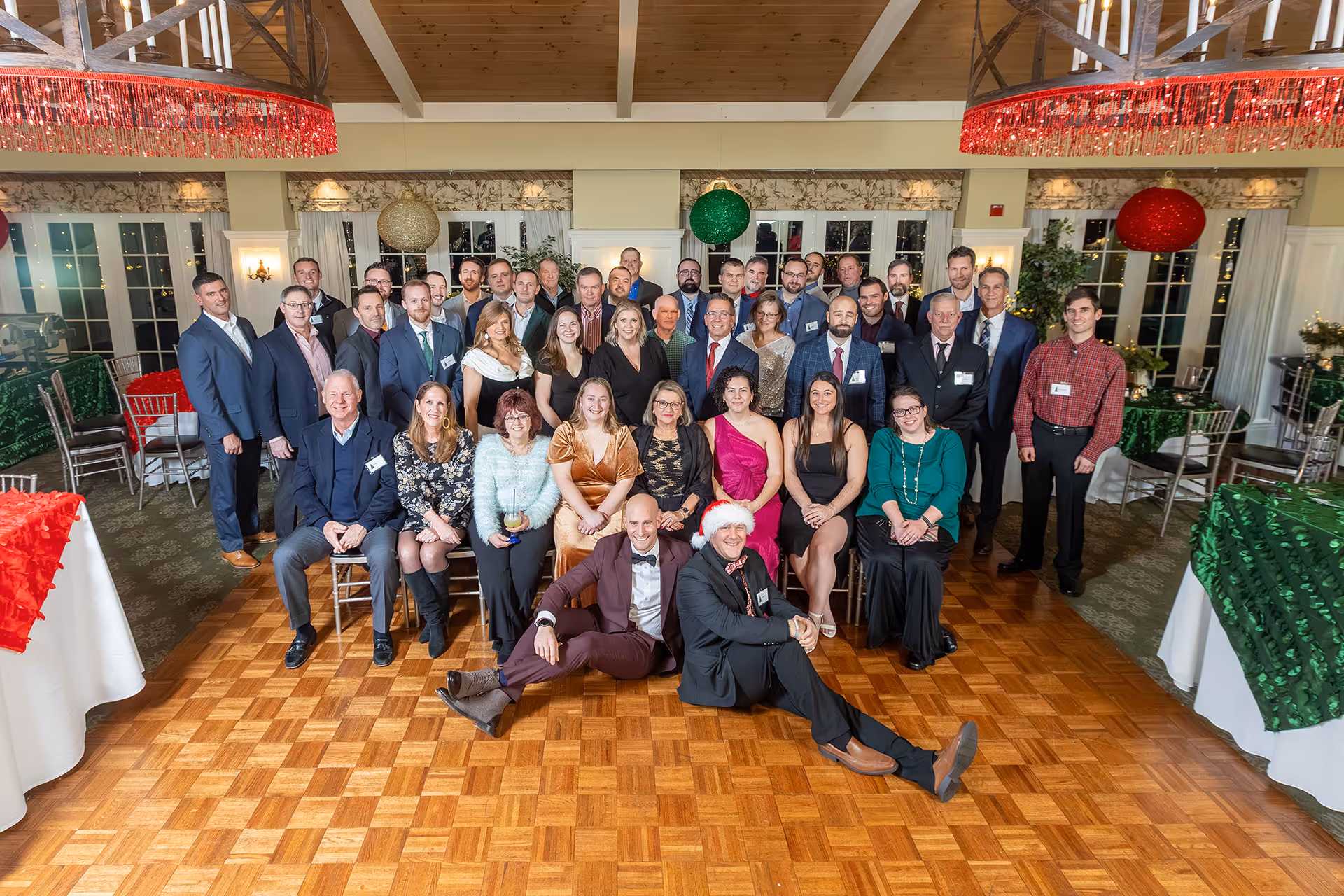 Large group of people posing at a festive indoor event with Christmas decorations and formal attire.
