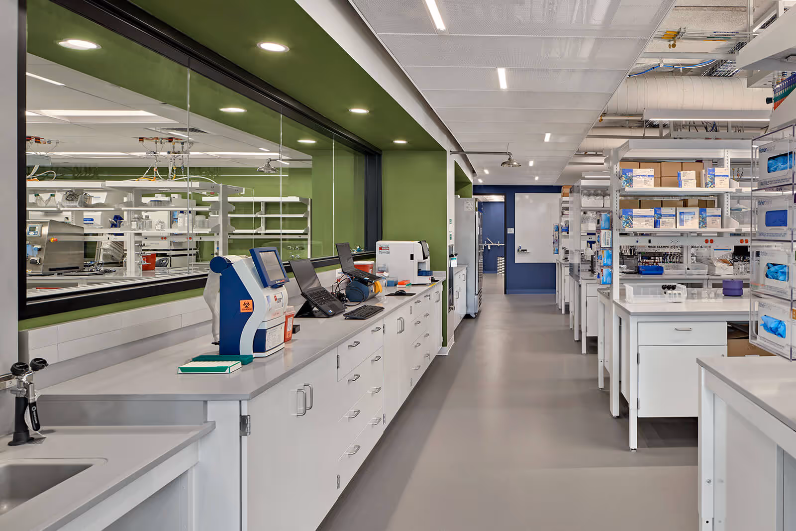 Modern scientific laboratory with white benches, equipment, and green walls