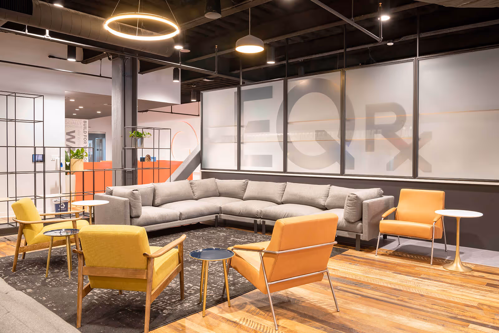 Modern office lounge with gray sectional, yellow and orange chairs