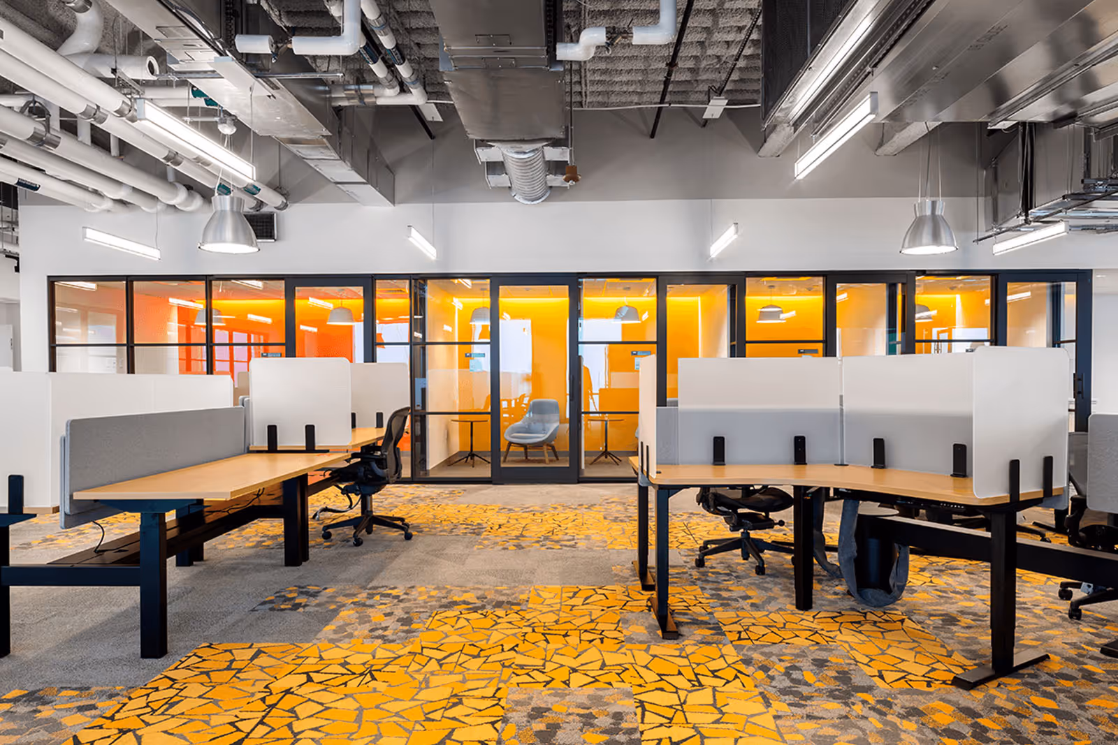 Modern office workspace with yellow carpet, glass partitions, and exposed ceiling
