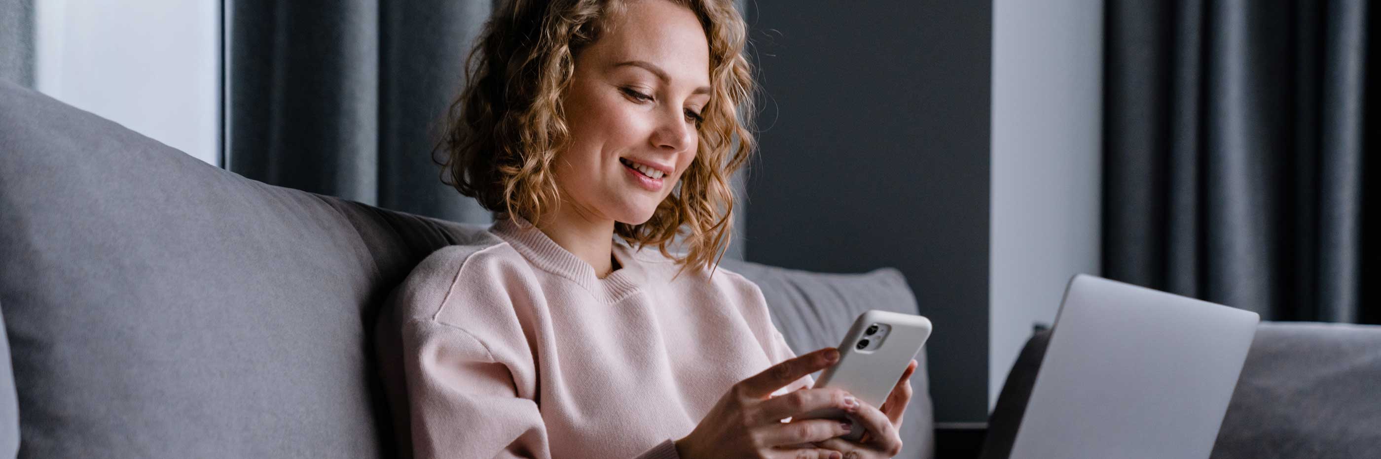 Woman smiling while using a smartphone on a couch.