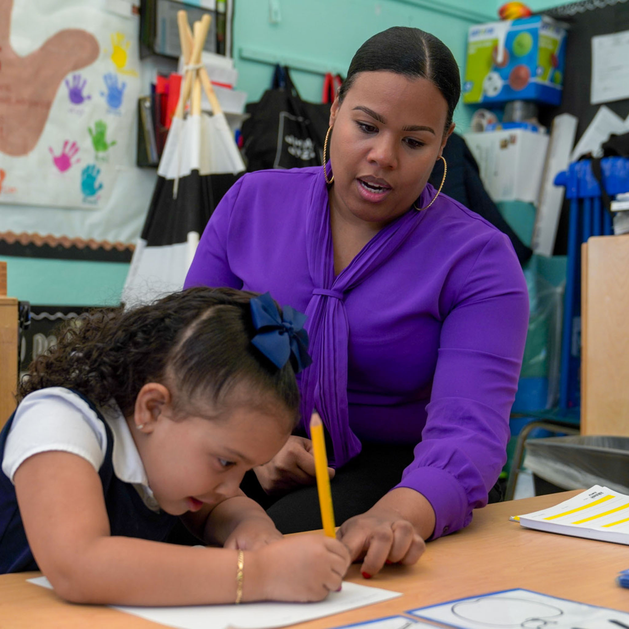 Teacher guiding young student writing at classroom desk