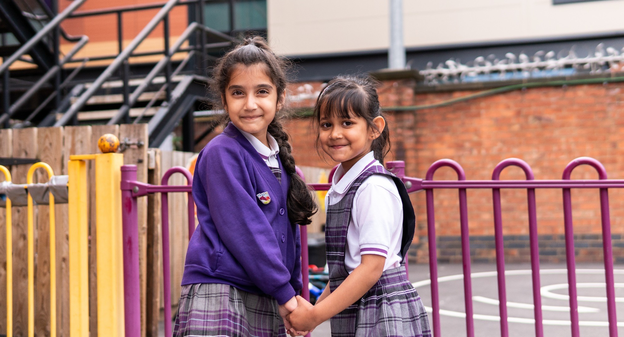 Two smiling girls in school uniform holding hands in playground