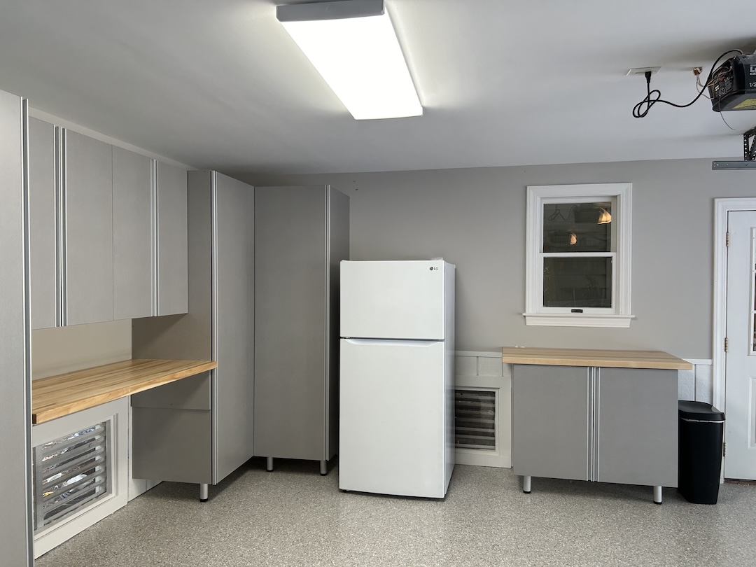 Gray car parked in a clean garage with white cabinets, drawers, and organized shelves along the back wall for optimal garage storage.