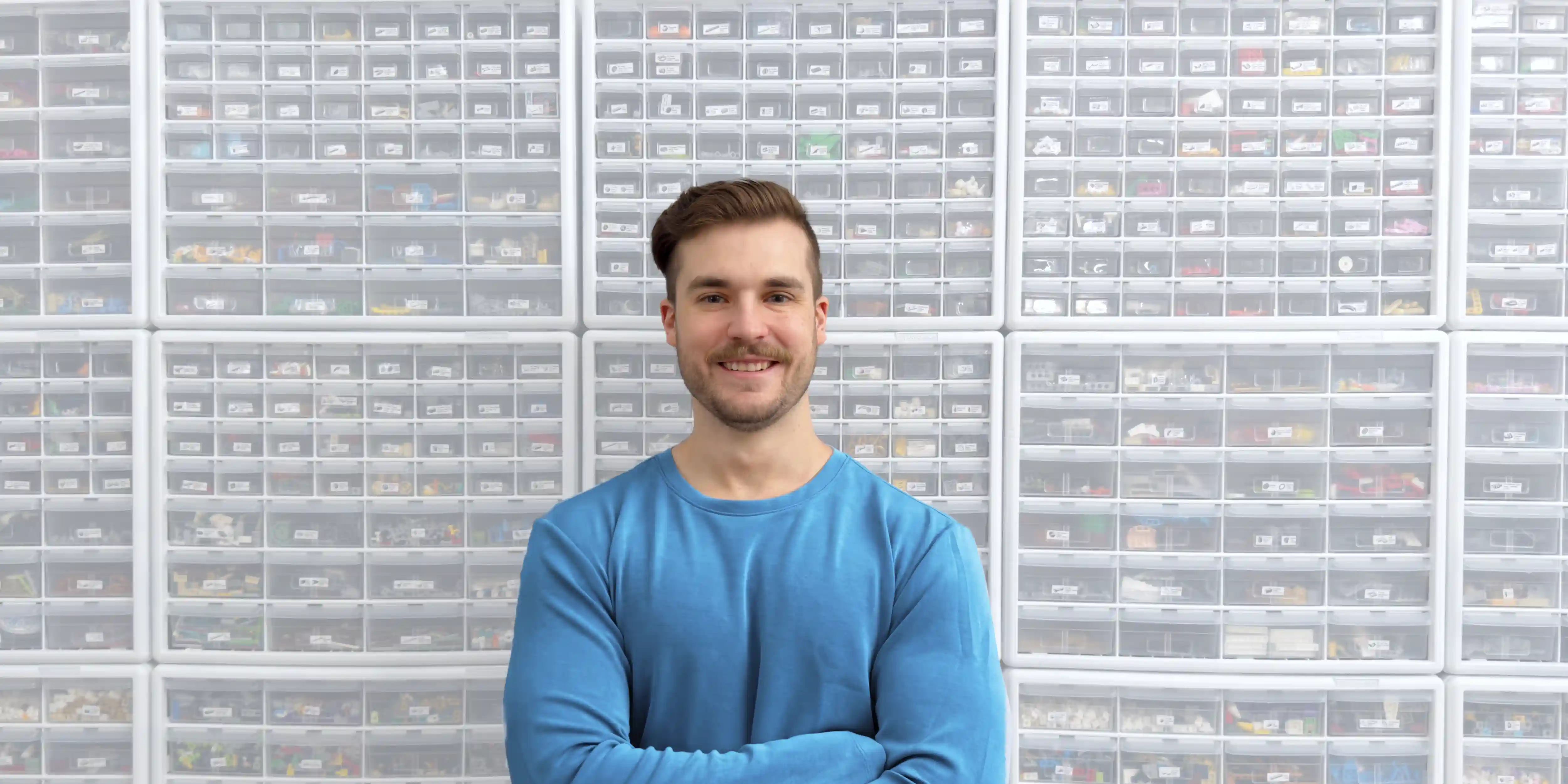 Ben Brickson poses against a wall of sorted LEGO