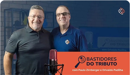 Banner promocional do programa 'Bastidores do Tributo', com os apresentadores Paulo Zirnberger e Orivaldo Padilha. Ambos estão em pé, sorrindo, em um estúdio de gravação com um microfone profissional em primeiro plano.
