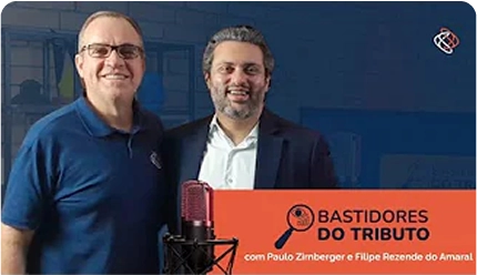 Banner promocional do programa 'Bastidores do Tributo'. A imagem mostra os anfitriões, Paulo Zirnberger e Filipe Rezende do Amaral, sorrindo juntos em um estúdio de gravação. Um microfone profissional está em primeiro plano.