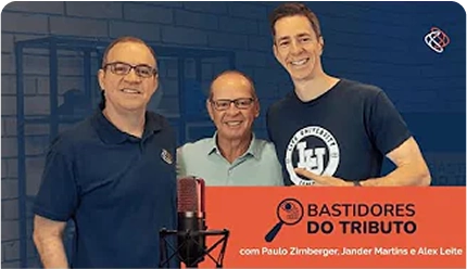 Banner promocional do programa 'Bastidores do Tributo' com os apresentadores Paulo Zirnberger, Jander Martins e Alex Leite. Os três homens estão juntos, sorrindo, em um estúdio de gravação com um microfone profissional em primeiro plano.