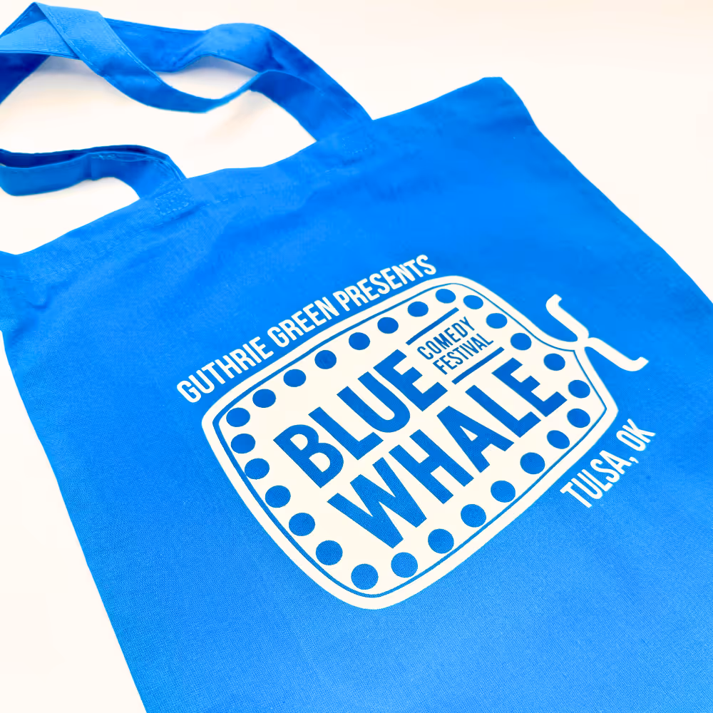 Bright blue tote bag featuring the Blue Whale Comedy Festival logo, printed with bold white ink for Guthrie Green Presents.