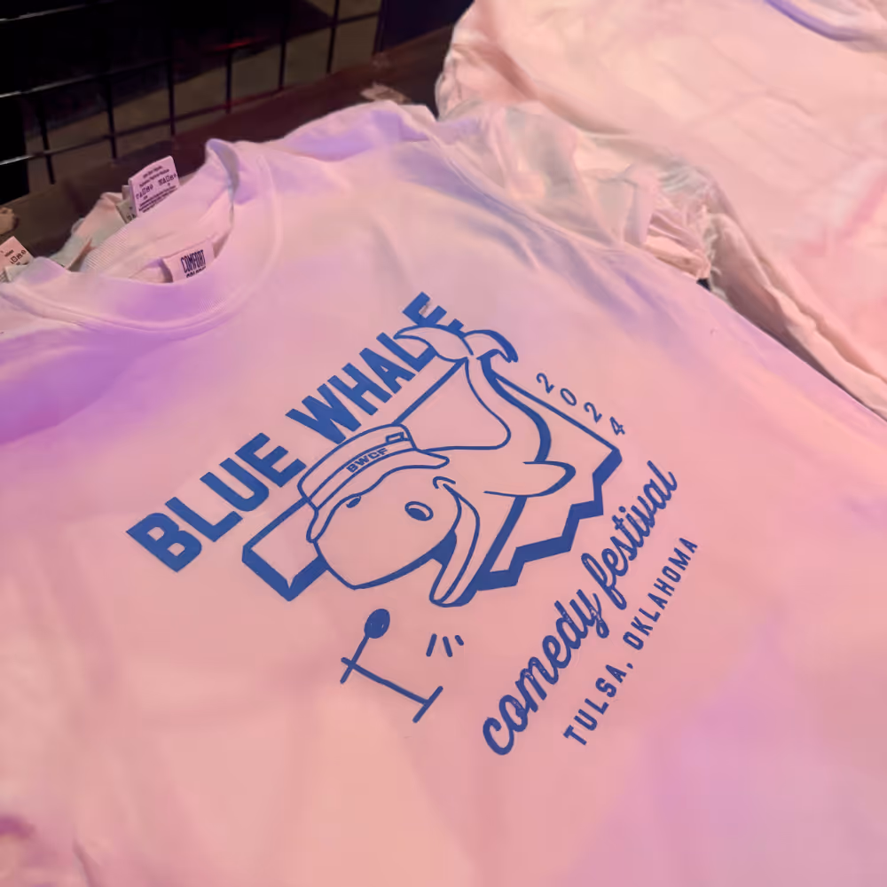 T-shirt with a playful blue whale graphic wearing a hat, created for the 2024 Blue Whale Comedy Festival in Tulsa, OK.