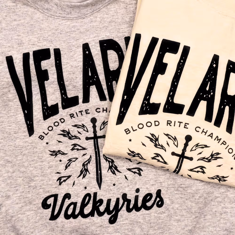 Velar t-shirts with sword and feather graphic in black ink on cream and gray shirts.