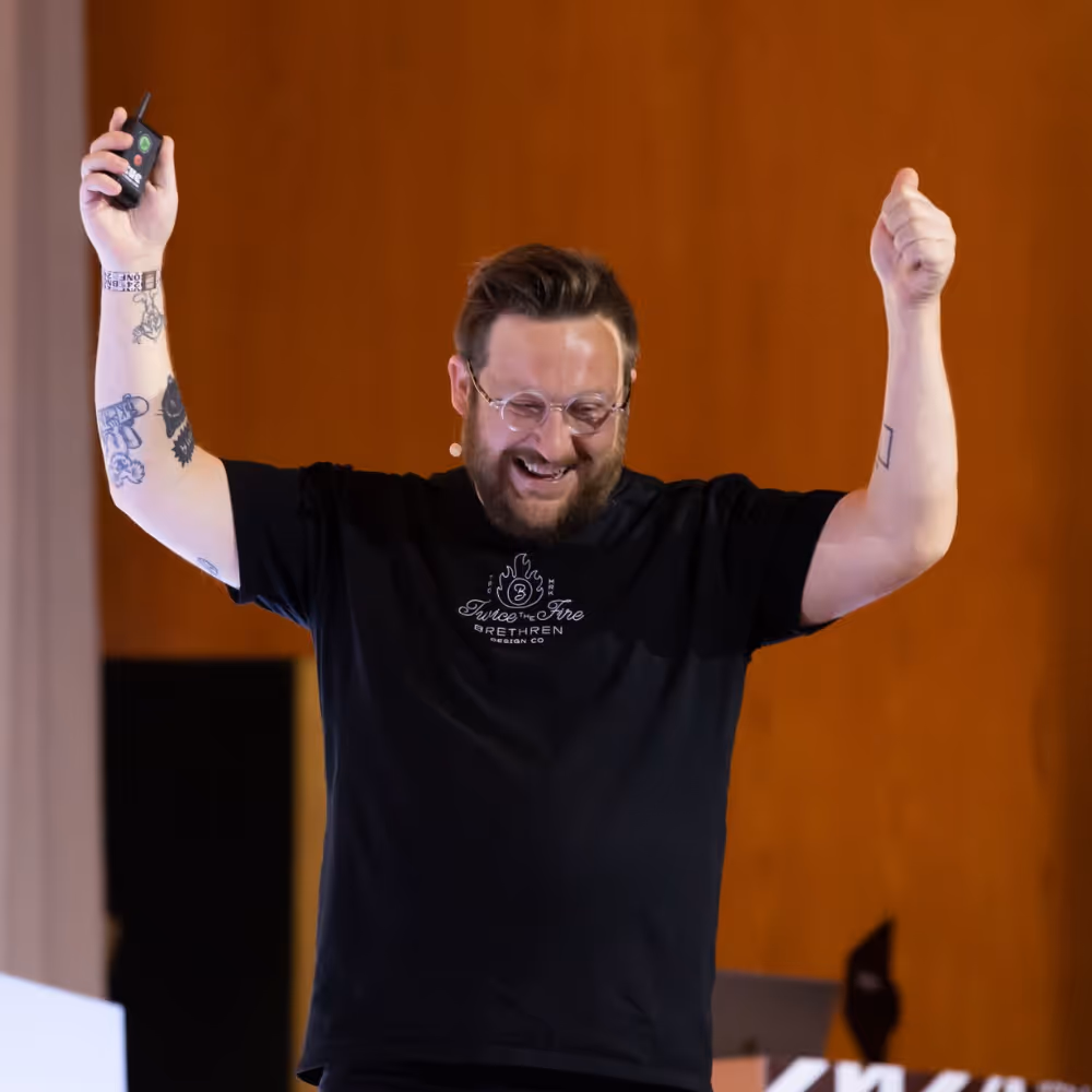 Man on stage wearing black Brethren Design Co shirt with "Twice the Fire" logo.