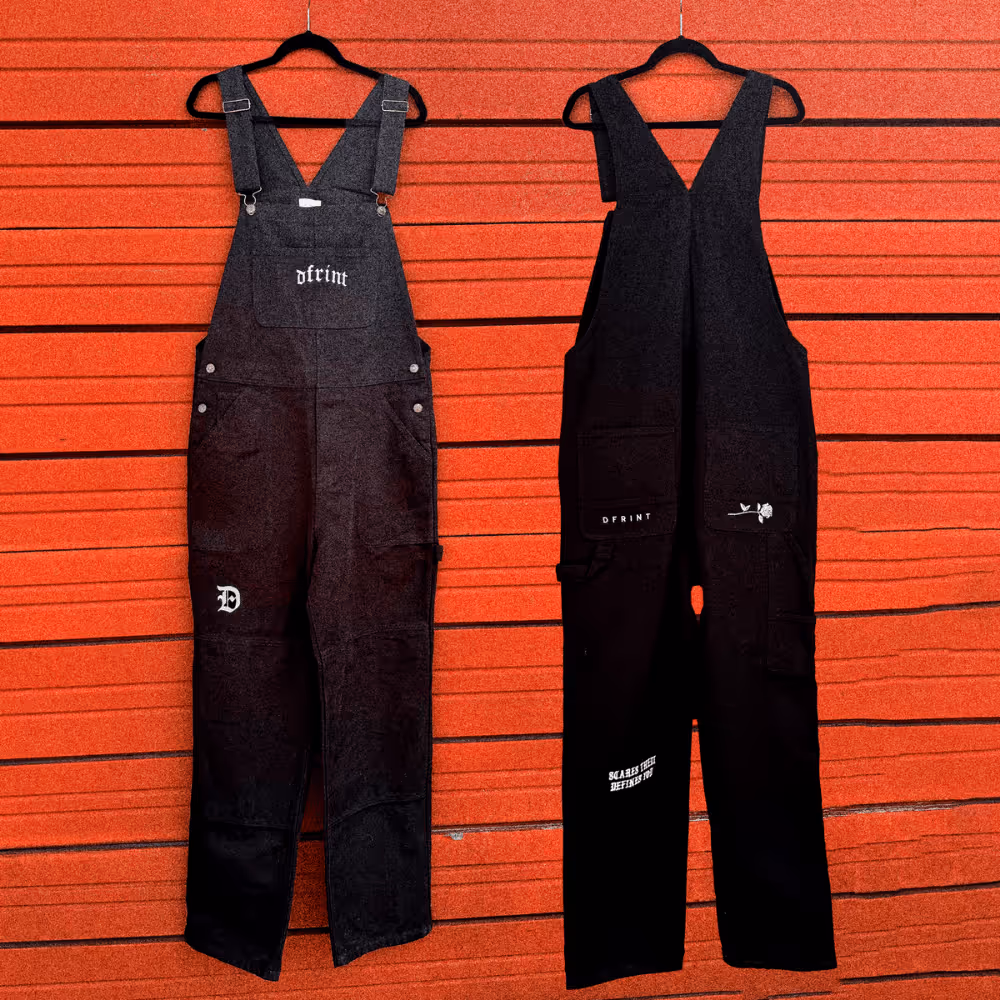 Two black DFRINT branded overalls with printed logos and graphics displayed against orange background.