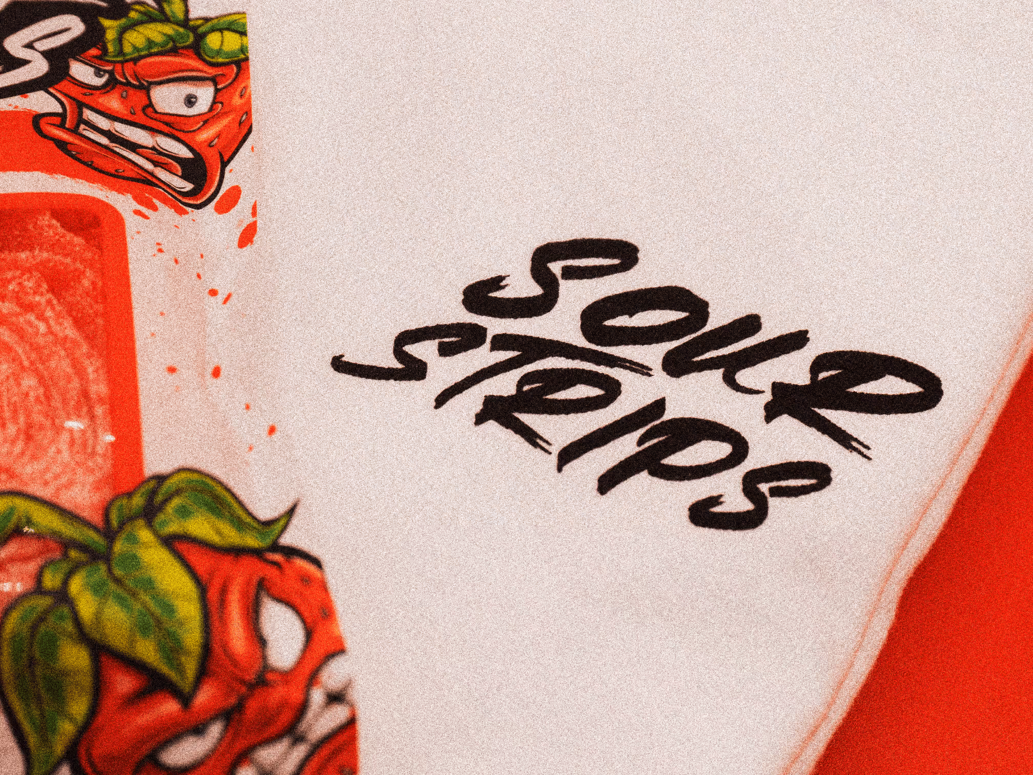 Close-up of Sour Strips logo and strawberry character printed on white t-shirt.
