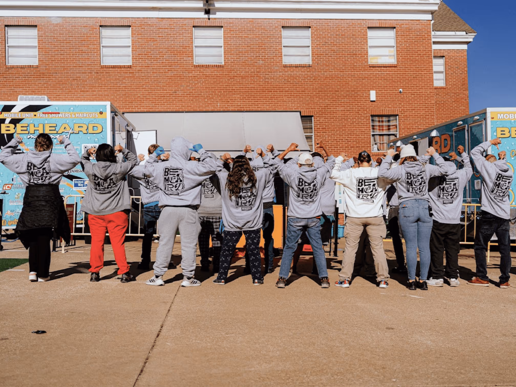 Group wearing custom BeHeard hoodies with backs facing camera at community event, printed by Prophecy Print & Design.