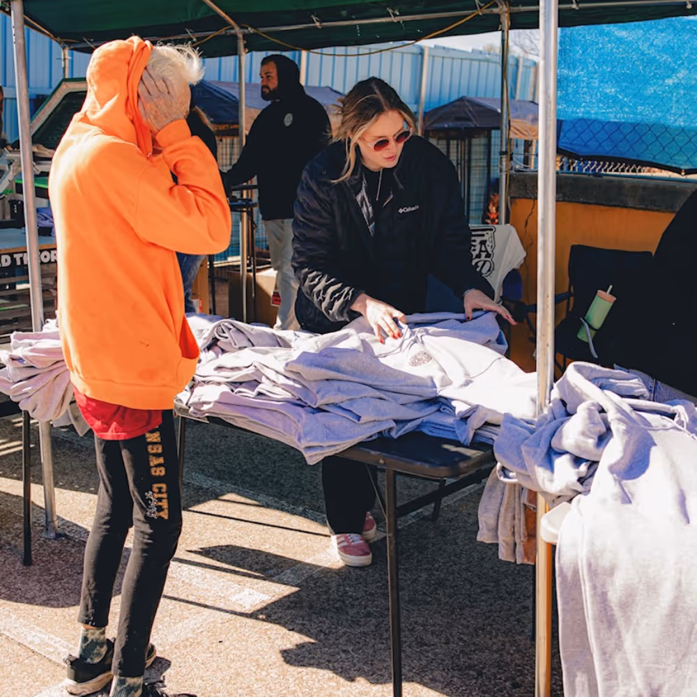 Prophecy Print & Design team member distributing BeHeard hoodies at live printing community event.