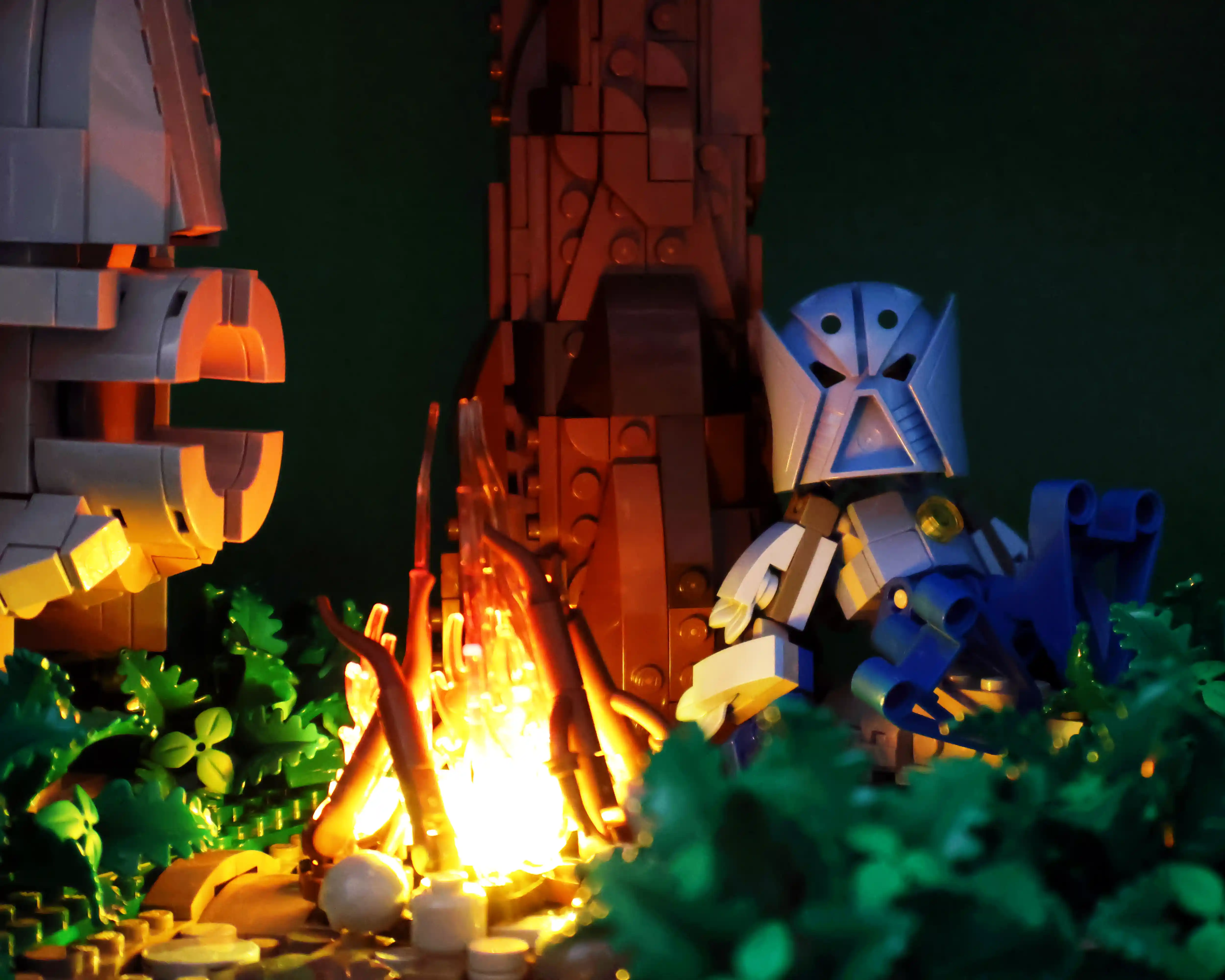 A custom build by Ben Brickson showcasing two matoran sit by a fire and share ghost storied underneath a large totem of a Bionicle beneath an even taller palm tree. 