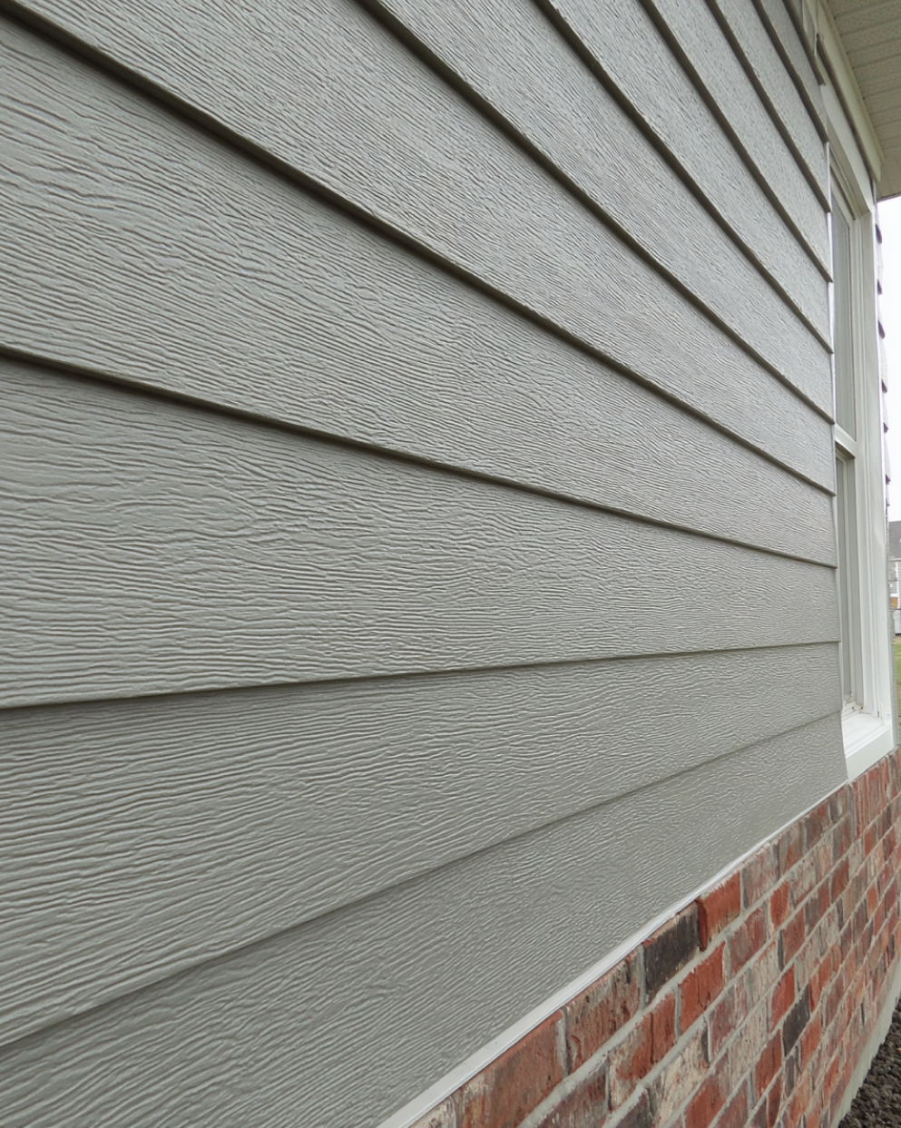 Close-up view of fiber cement siding installed on a house exterior above a brick foundation.