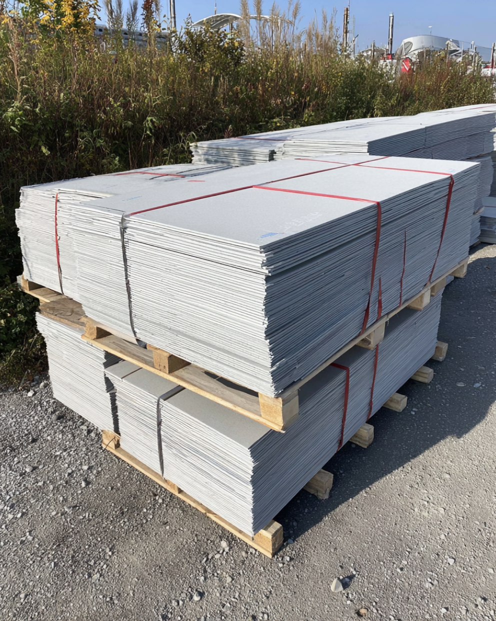 Stacks of gray fiber cement siding boards neatly piled on wooden pallets outdoors.