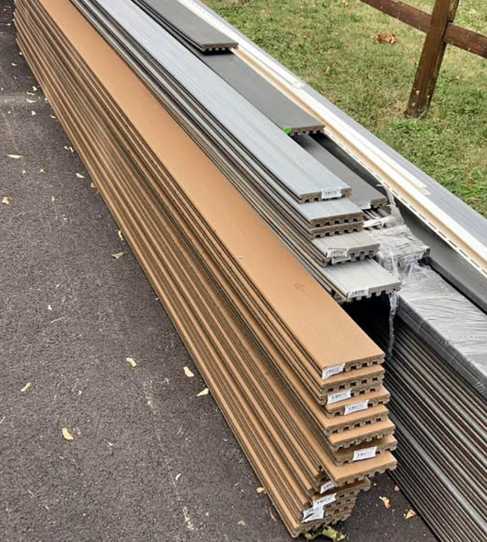 Gray and brown composite decking boards stacked on driveway – Mixed color composite decking planks stacked on the ground, prepared for home improvement.