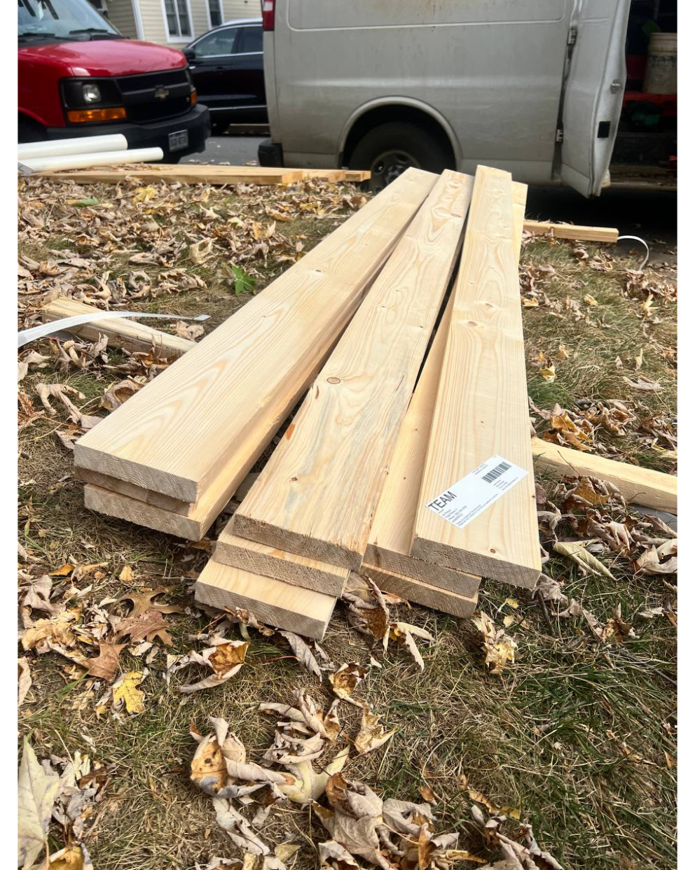 Stack of lumber boards on grass with work van in background – construction wood supply