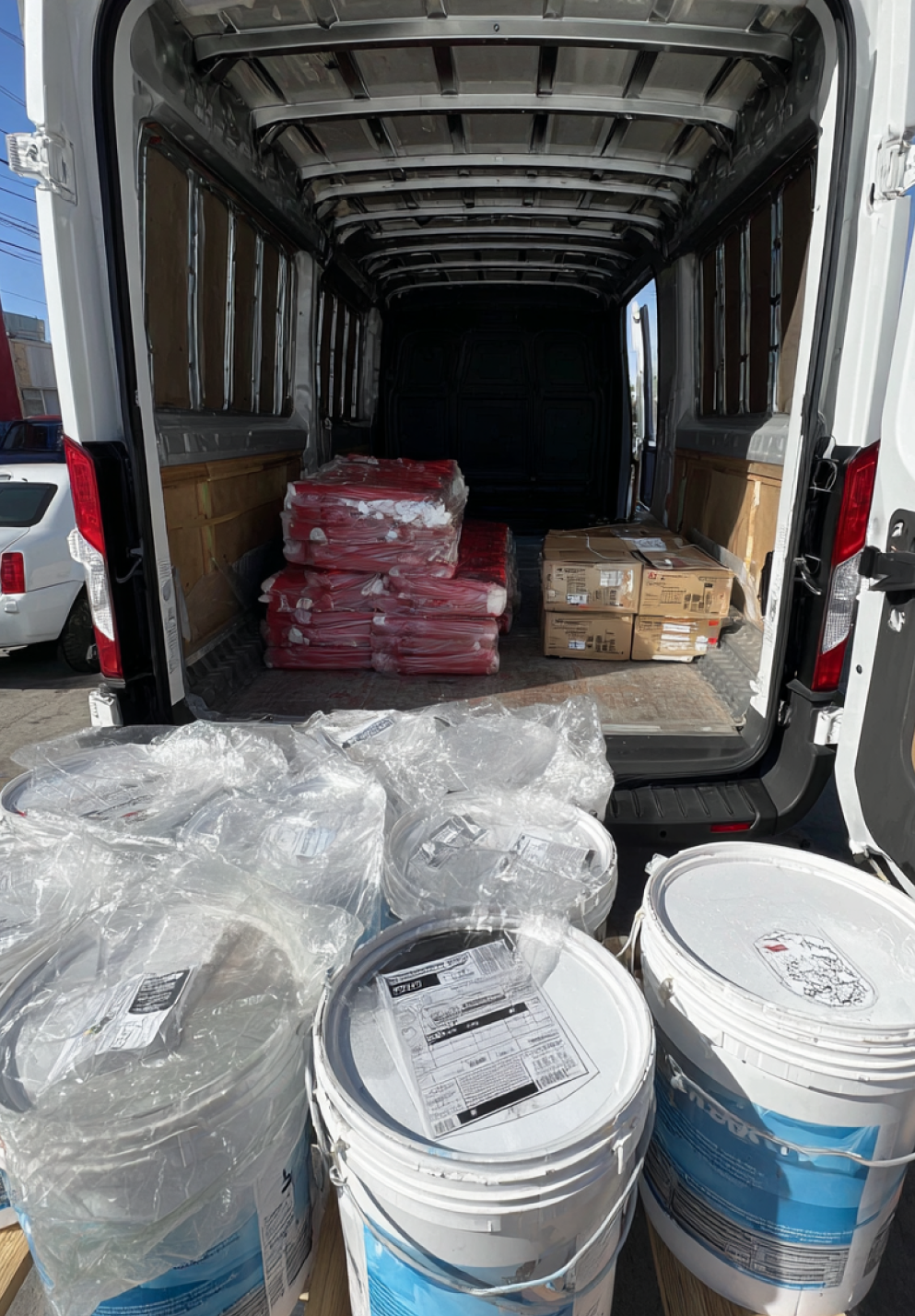 White cargo van interior with pallets of paint buckets and wrapped building materials.