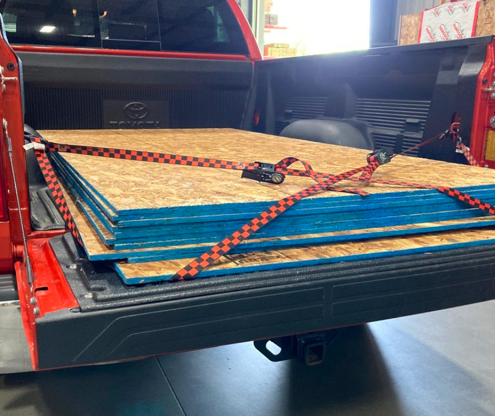 OSB plywood sheets with blue edges secured with red and black checkered straps in a red Toyota pickup bed