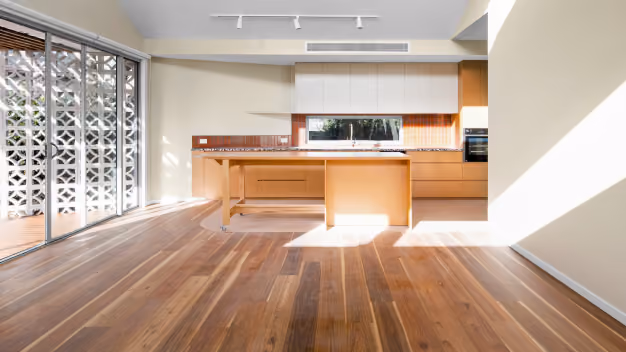 Modern kitchen with wooden floor, orange cabinets, island, and sliding glass doors letting in sunlight.