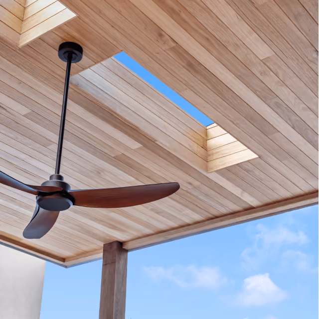Wood-paneled ceiling with skylights and a modern ceiling fan against a clear blue sky.