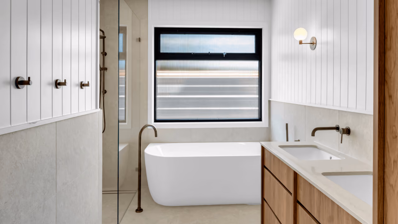 Modern bathroom with freestanding tub, double sinks, wood cabinets, and frosted window.