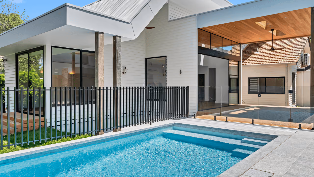 Modern house patio with a swimming pool, wooden ceiling, large windows, and glass pool fencing.